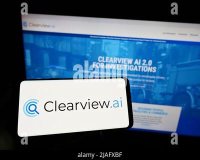 Person holding mobile phone with logo of facial recognition company Clearview AI Inc. on screen in front of web page. Focus on phone display. Stock Photo