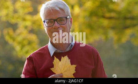 Medium closeup of senior grey-haired man holding a yellow leaf park nature background copy space outside . High quality photo Stock Photo