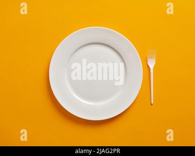 Empty or blank white plate with plastic fork on yellow background. Stock Photo