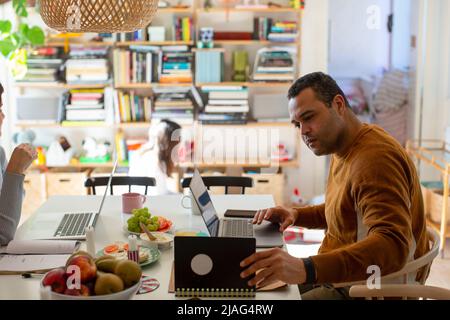 Side view of male freelancer checking diary while working on laptop at home Stock Photo