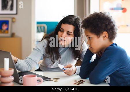 Mother teaching online payment to son on laptop at home Stock Photo