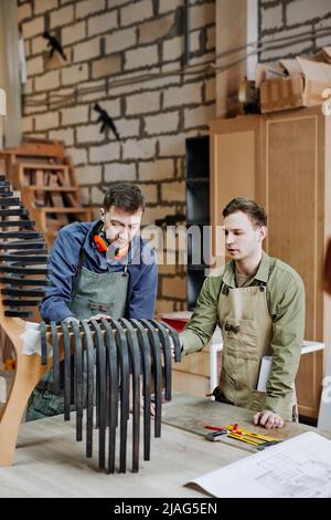 Vertical portrait of two carpenters working on handcrafted piece of furniture in workshop Stock Photo