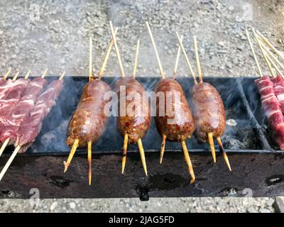Appetizing sausages and meat skewers grilled over the fire as they cook outdoors during a barbecue Stock Photo