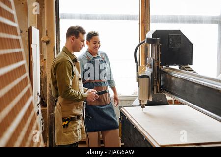 Side view portrait of two carpenters operating CNC laser machine in automated woodworking production Stock Photo