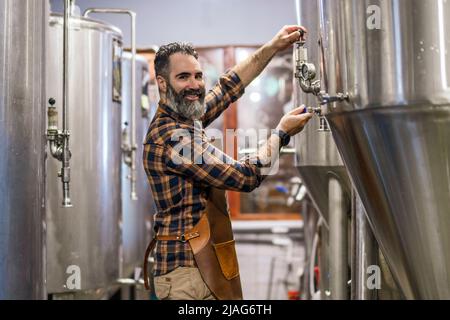 Man is working at craft beer factory. He is operating machinery in brewery. Small family business, production of craft beer. Stock Photo