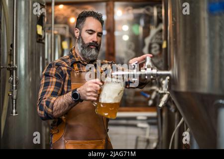 Bearded brewery master tasting beer in production facility. Small family business, production of craft beer. Stock Photo
