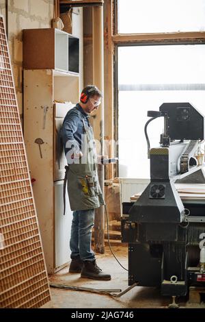 Full length portrait of male carpenter operating wood cutting machine in automated production workshop Stock Photo