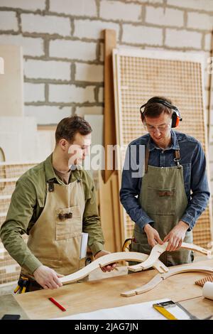 Vertical portrait of two workers fitting furniture parts while building handcrafted piece in carpentry workshop Stock Photo