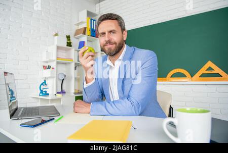 cheerful school teacher in classroom having lunch break with apple Stock Photo