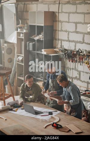 Vertical shot of modern artisans designing handcrafted furniture piece in carpenters workshop Stock Photo