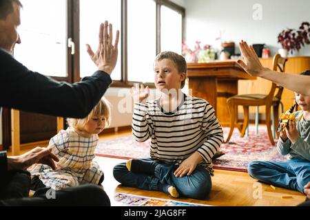 Parents doing high-five with son having down syndrome sitting in living room at home Stock Photo