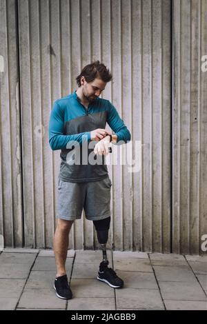 Young man with disability checking time while standing on footpath against wall Stock Photo