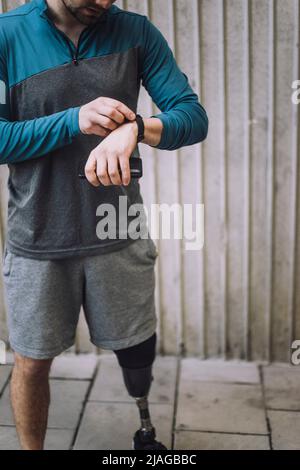Man with disability checking time on smart watch while standing on footpath Stock Photo