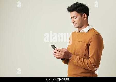 Serious young Indian entrepreneur checking messages from colleagues on smartphone Stock Photo
