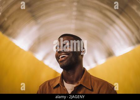 Young man laughing with eyes closed in illuminated tunnel Stock Photo