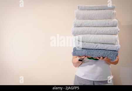 Woman holding a stack of clean white bath towels on light background Stock Photo