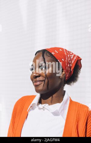 Smiling young woman in bandana standing against wall during sunny day Stock Photo