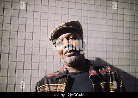 Portrait of smiling mature man wearing flat cap standing against wall Stock Photo
