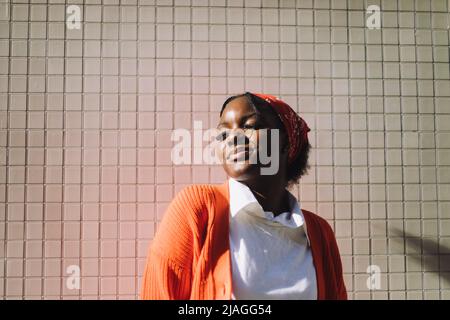Smiling woman wearing bandana standing with eyes closed against wall Stock Photo