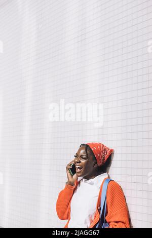 Young woman laughing while talking on mobile phone against wall Stock Photo
