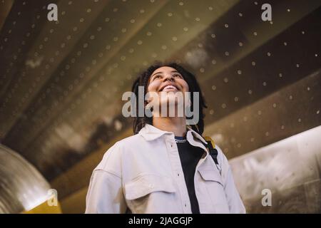 Happy young genderqueer person looking up while standing in subway Stock Photo