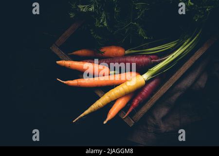 Colorful Rainbow carrot with their green leaves in a box on wooden background, top view Stock Photo
