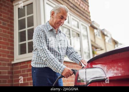 Mature Man Attaching Charging Cable To Environmentally Friendly Zero Emission Electric Car At Home Stock Photo