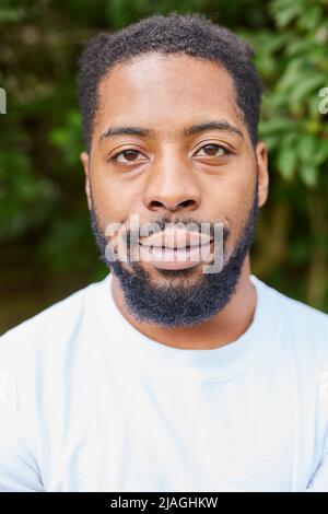 Head And Shoulders Portrait Of Smiling Young Man Standing Outdoors In Garden Stock Photo