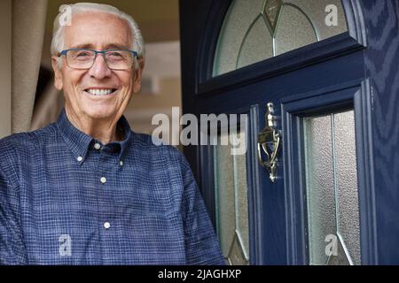Portrait Of Smiling Senior Man Standing At Open Front Door Of House Stock Photo