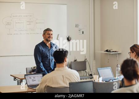 Smiling male professor looking at students in classroom Stock Photo