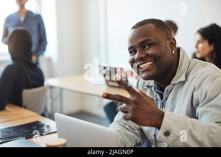 Portrait of happy male student showing peace sign while sitting in classroom Stock Photo