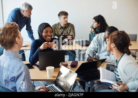 Smiling female student discussing with friends while sitting in classroom Stock Photo
