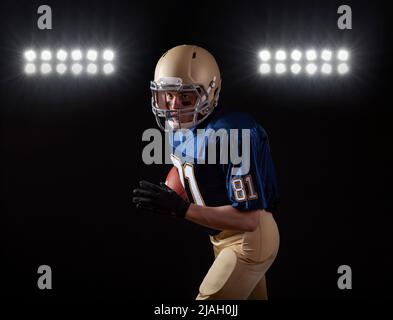 Young football player in running action on a dark background with stadium lights Stock Photo