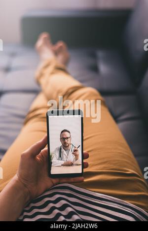 Woman lying on a sofa and talking with a doctor online using mobile phone. Telemedicine concept. Stock Photo