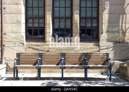 wooden bench next to stone walkway in front of old building with decorative architecture Stock Photo