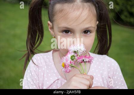 close-up portrait of a cute girl 6-7 years old with a small bouquet of daisies flowers. A little girl with a dreamy look smells flowers. Stock Photo