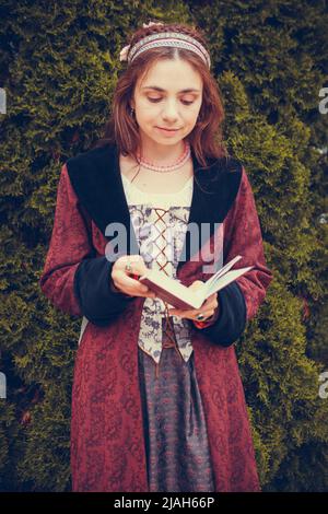 Portrait of brunette woman dressed in historical Baroque clothes  reading book, outdoors. Middle class medieval dress