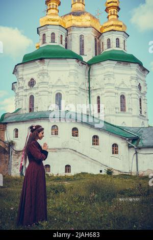 Portrait of brunette woman praying, dressed in historical Baroque clothes, outdoors. Middle class medieval dress