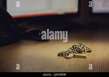A bunch of keys to the room lies on an office desk with computer monitors Stock Photo
