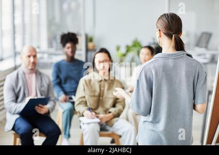 Back view of female coach giving lecture or seminar in office to diverse group of people, copy space Stock Photo