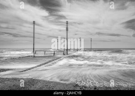 Waves crashing over an outflow pipe with marker posts Stock Photo