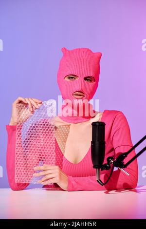 Unrecognizable young female influencer wearing pink sweater and balaclava holding bubble wrap prepared for ASMR content Stock Photo