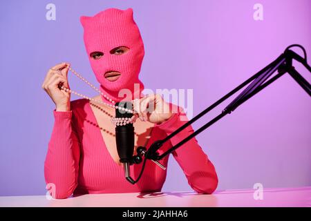Unrecognizable young female influencer wearing pink sweater and balaclava recording ASMR content using bead necklace Stock Photo