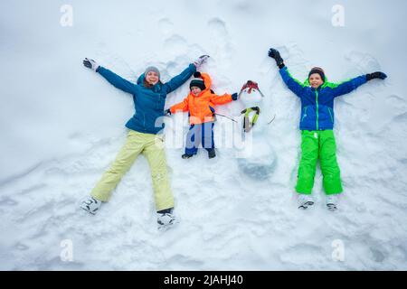 Mother and two boys lay in the snow with snowman view from top Stock Photo