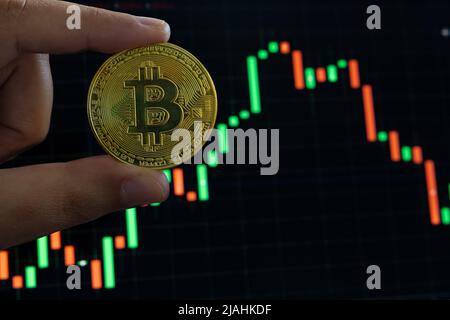 Bitcoin or cryptocurrency. Losing money on cryptocurrency markets concept photo. Man holds a bitcoin against the charts. Selective focus on foreground Stock Photo