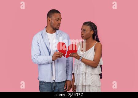 Disappointed couple holding two pieces of broken red paper heart Stock Photo