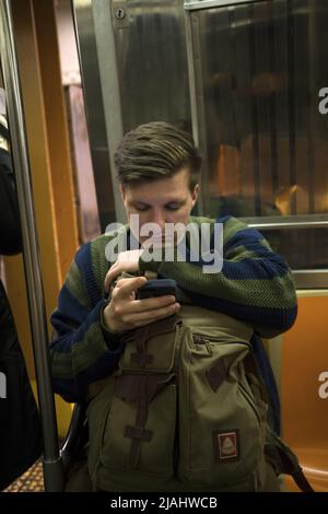 Young man reading on his phone while riding a subway train in Brooklyn, NY. Stock Photo
