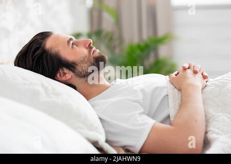 Lonely young laying in bed alone, staring at ceiling Stock Photo