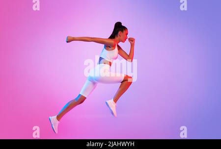 Sporty Lady Running In Mid Air Over Pink Neon Background Stock Photo