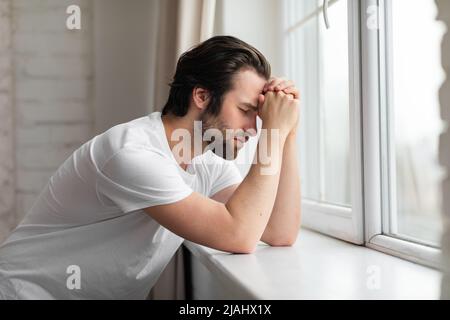 Thoughtful millennial guy standing next to window at home Stock Photo